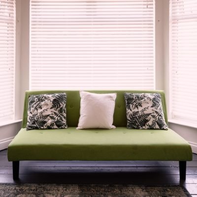 A vibrant green sofa with pillows against white windows.