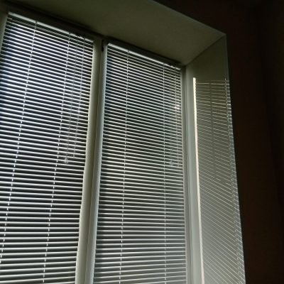 White horizontal blinds on the window block out the bright sunlight. shadow from the blinds
